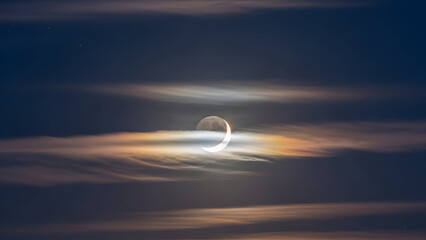 Crescent Moon Partially Obscured by Wispy Clouds During Evening Sky Observation