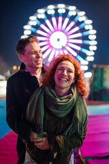 Happy couple embracing, laughing at amusement park at night