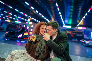 Couple sharing drink at bumper car funfair night