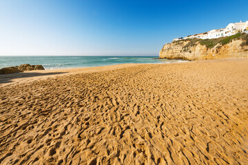 The sandy Praia de Carvoeiro beach with the Alto da Praia do Carvoeiro upper town of whitewashed buildings above in Carvoeiro, Portugal, Algarve region.
