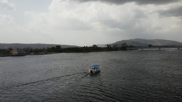 Aerial drone footage of Ghana, Africa, serene lake surrounded by mountains. Traditional boats across the water near a local village, with views near the Right to Dream Football Academy