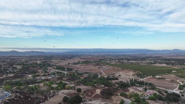 Early morning drone flight over a beautiful vineyard in Temecula, California while hot air balloons soar through blue skies.