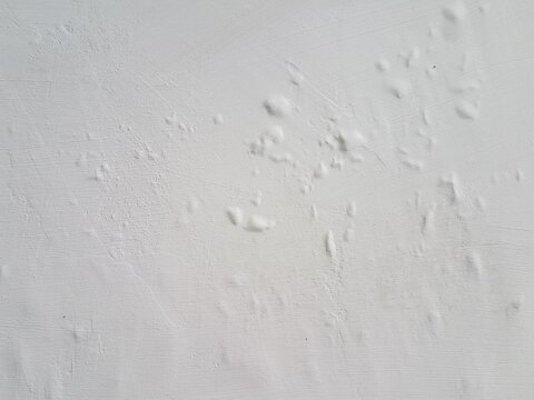 Detail of a white painted wall showing small blisters and bumps. Water damage and bubbling paint texture on a white interior wall. Abstract background of deteriorating paint and swollen plaster.