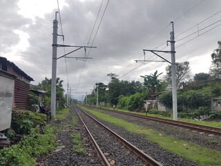 Double railway tracks extending toward the horizon. Utility poles stand beside the tracks under a cloudy sky. View of transportation
