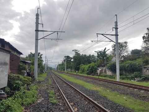 Double railway tracks extending toward the horizon. Utility poles stand beside the tracks under a cloudy sky. View of transportation