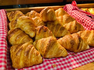 freshly baked golden croissants in a wooden tray with red checkered cloth