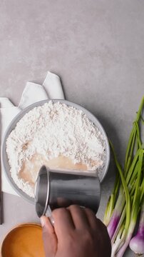 Overhead view of water being added to flour to make scallion pancake dough, top view of cong you bing dough being mixed, process of making scallion pancakes