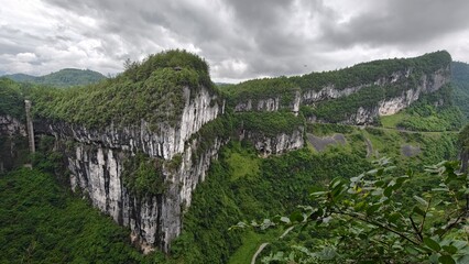 Breathtaking view of towering limestone cliffs and dense green vegetation at the Wulong Karst National Geological Park under a dramatic cloudy sky
