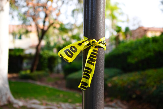 Yellow caution tape tied to a pole in a park in Corona, California, symbolizing restricted access, public safety, and temporary closure.