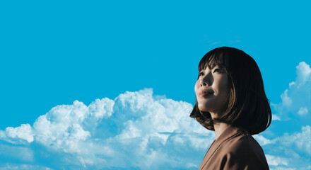春・上を見上げ微笑む明るい表情の日本人女性の顔　前向きでポジティブ希望に満ちた表情　就職・新生活・旅行・リラックス・入学のイメージ　青空と雲の背景