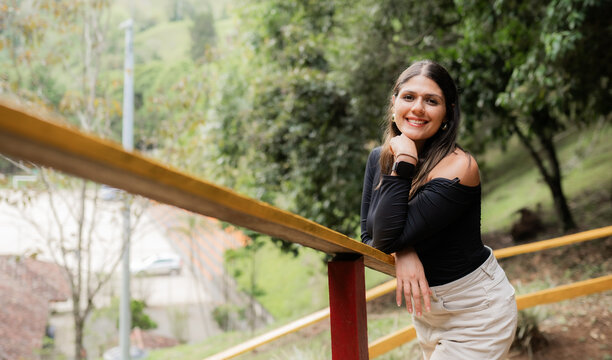 Joven sonriente apoyada en baranda de madera en parque natural urbano