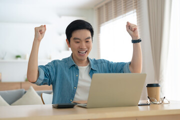 Funny euphoric young asian man celebrating winning or getting ecommerce shopping offer on computer laptop. Excited happy boy winner looking at notebook celebrating success