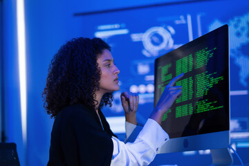Young woman working intently on computer in high-tech office with digital data display at night