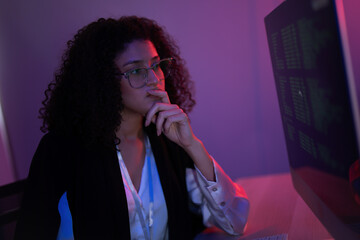 Woman focused on computer screen in a dimly lit room while analyzing data at night