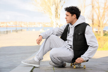 Young man in grey sports suit sitting on skateboard outdoors