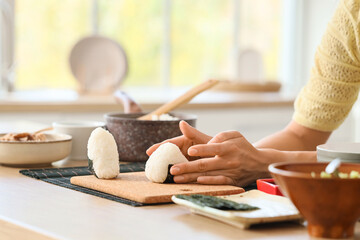 Obraz premium Young woman preparing traditional Japanese onigiri on table in kitchen, closeup