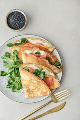 Crepes or thin pancakes with lightly salted salmon, soft cheese and cornsalad