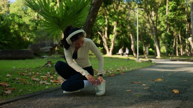 Female runner with headphones feeling sudden ankle pain and stopping her workout. Athlete suffering from a sprained ankle during a run