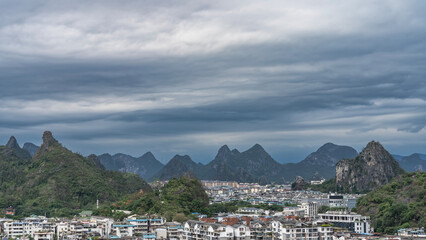 Beautiful urban landscape. There are many multi-storey buildings surrounded by mountains. Green vegetation. Picturesque mountain peaks against the sky and clouds. China. Guilin.
