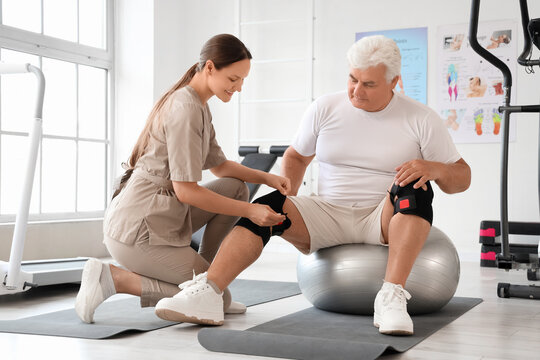 Senior man with therapist putting on knee pads in rehabilitation center