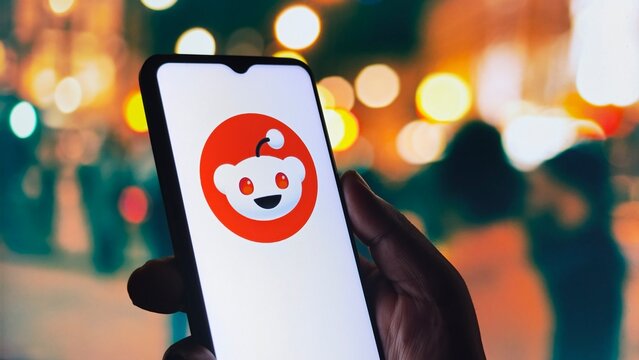 Closeup of reddit application logo displayed on a smartphone screen held in a hand at night