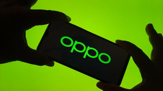 Hands holding a smartphone displaying the glowing green oppo logo against a bright green background