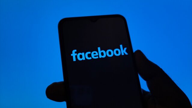 Close up of facebook logo displayed on a smartphone screen held in a hand against a bright blue background