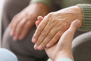 Woman holding grandmother's hand at home, closeup