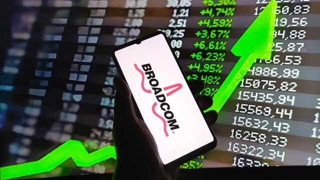 Hand holding smartphone displaying broadcom logo against stock market data and rising green arrow