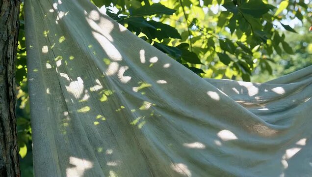 elegant lifestyle 4K shot of flowing fabric softly illuminated by dappled sunlight filtering through leaves creating organic shadow patterns that evoke calm design aes tics and premium interior