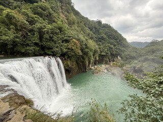Shifen Waterfall Taiwan: Scenic waterfall cascading over rocks into a pool surrounded by lush tropical vegetation in Shifen.