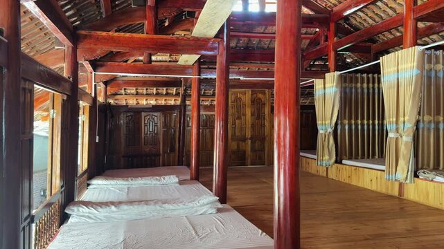 Wide interior view of a traditional Bac Ha homestay dormitory with wooden beams, floor mattresses and curtained sleeping bays inside a rustic hill tribe stilt house.