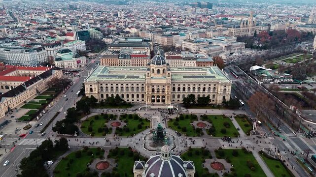 Aerial landscape drone shot panning toward and over the Austrian Natural History Museum in Vienna, capturing its grand fa&ccedil;ade, surrounding streets, and city buildings under clear daylight.