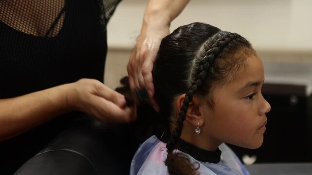 Hairdresser styling a young girl's braids with hair extensions in a salon
