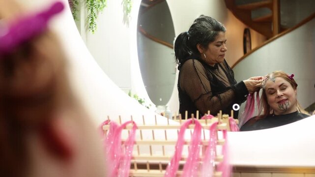 Hairdresser braiding pink hair extensions on a woman with a moko kauae tattoo