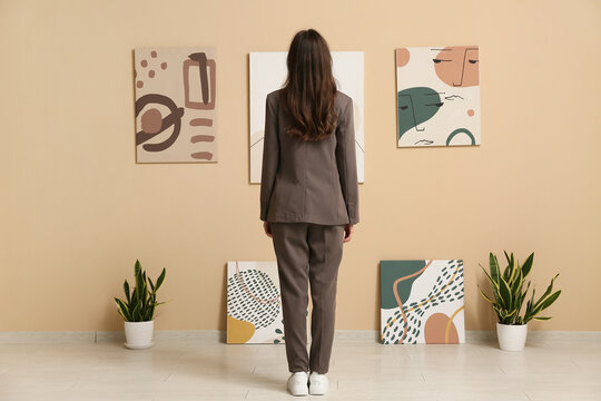 Young woman near paintings on beige wall in art gallery, back view