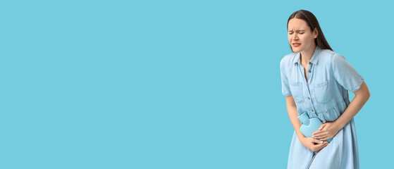 Young woman with hot water bag on blue background. Cystitis concept