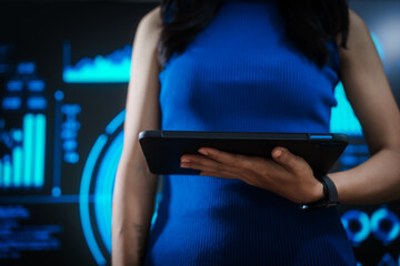 Woman holding tablet computer with futuristic blue data dashboard background, digital analytics, smart technology, data visualization, business intelligence, advanced user interface design.