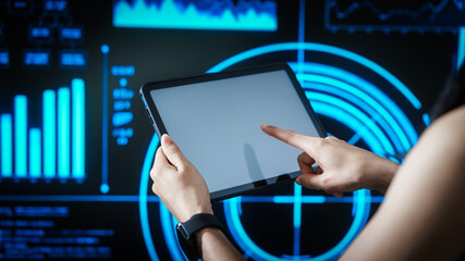 Woman holding tablet computer with futuristic blue data dashboard background, digital analytics, smart technology, data visualization, business intelligence, advanced user interface design.