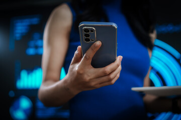 Professional woman multitasking with smartphone and laptop amid futuristic blue data dashboards, illustrating digital transformation, smart technology, productivity, advanced innovation.