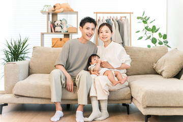 Smiling family holding a baby sitting on a sofa in their home, family, parent and child