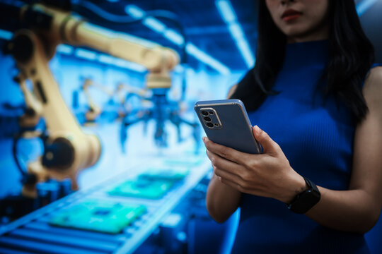 Woman using smartphone inside automated factory with robotic arms and production line, representing smart manufacturing, industry innovation, industrial automation, modern manufacturing.