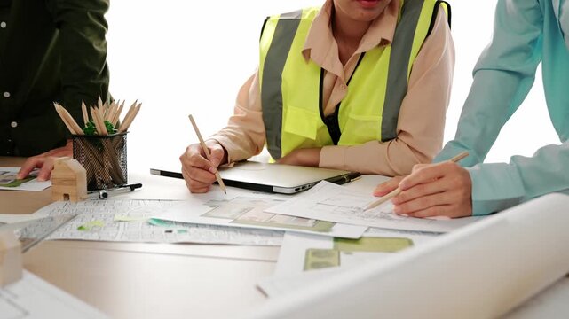 Smart architect and safety engineer discussion about building blueprint on table with architectural document, measurement tools and wooden block scatter around at modern office. Closeup. Delineation.