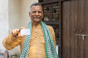 Senior rural Indian farmer holding debit, credit or bank card. Happy male showing blank Identity...