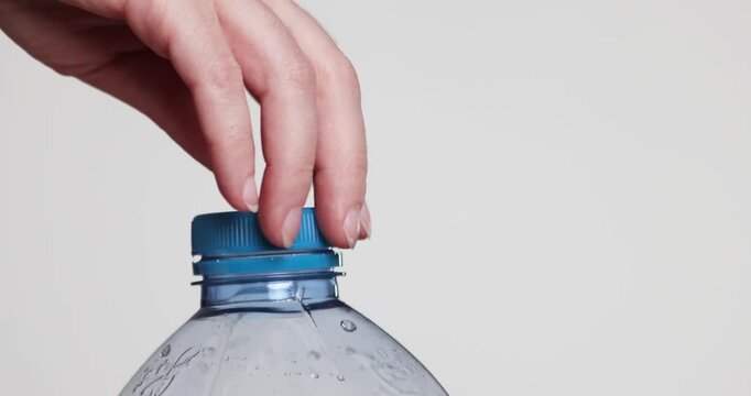 plastic cap of water bottle is opened by female hands on light background close-up
