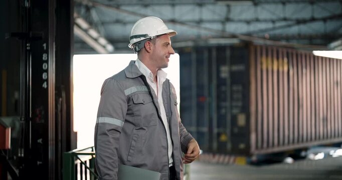 caucasian male logistics worker holding laptop and giving thumbs up gesture while standing near open cargo container and forklift during warehouse operations and shipping process