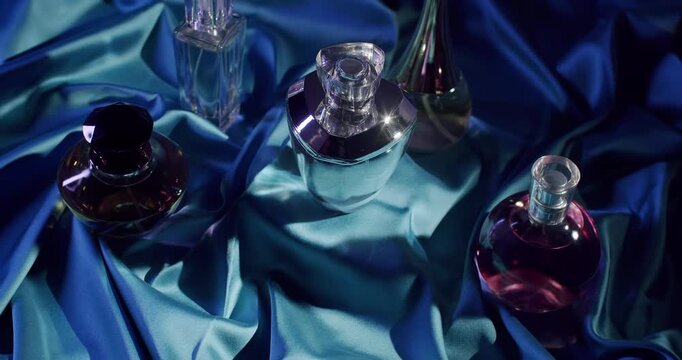 A collection of elegant perfume bottles arranged on luxurious blue satin fabric under dramatic lighting, highlighting the beauty and sophistication of the glass containers and their contents.