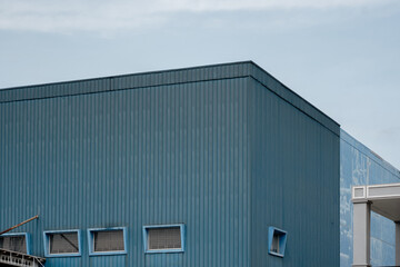 Obraz premium Corner view of blue industrial factory building with corrugated metal siding. Minimalist warehouse exterior architecture design against sky.