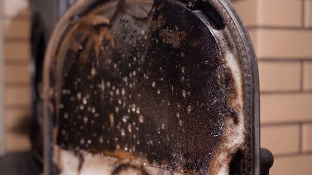 A sooty fireplace window is sprayed with cleaning agent