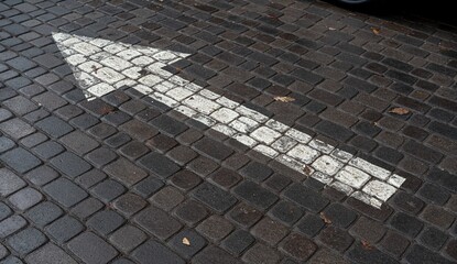 A white arrow painted on a cobblestone street, indicating direction. The surface shows signs of wear and fallen leaves.
